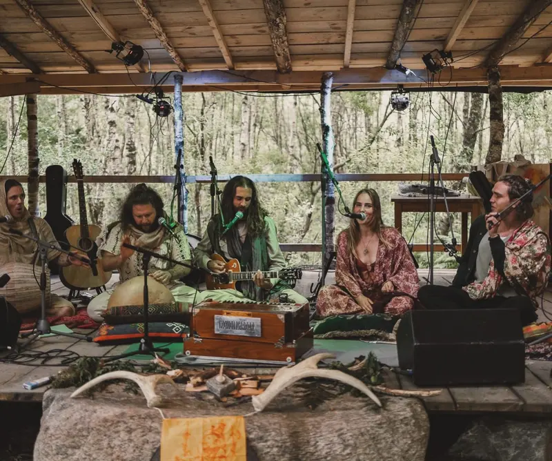 Familjen Kirtanen sjunger på en scen i skogen, med harmonium, gitarr och trumma.